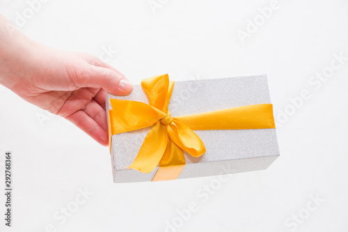 female hand holds a gift box with a gold bow photo