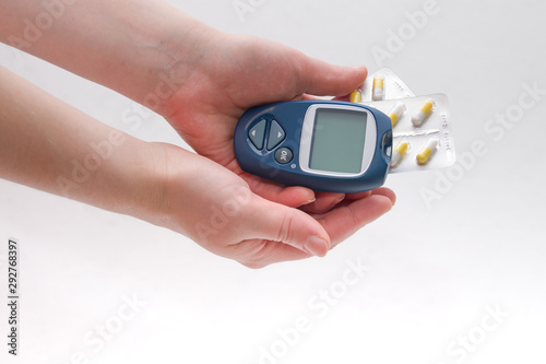 female hand holds a blue glucometer and several packs of tablets of capsules in long colors