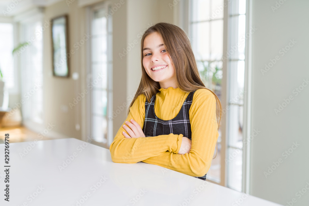 Beautiful young girl kid sitting on the table happy face smiling with crossed arms looking at the camera. Positive person.