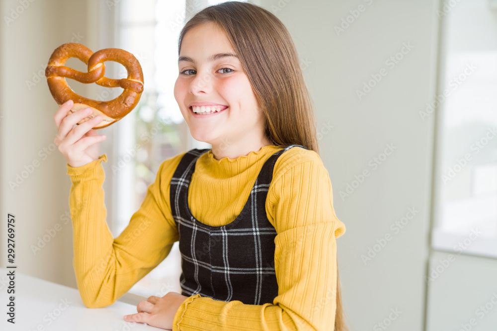 Beautiful young girl kid eating german snack salty pretzel with a happy face standing and smiling with a confident smile showing teeth Beautiful young girl kid eating german snack salty pretzel with a happy face standing and smiling with a confident smile showing teeth
