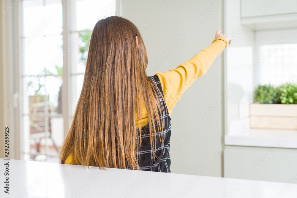 Young beautiful blonde kid girl wearing casual yellow sweater at home Posing backwards pointing ahead with finger hand Young beautiful blonde kid girl wearing casual yellow sweater at home Posing backwards pointing ahead with finger hand