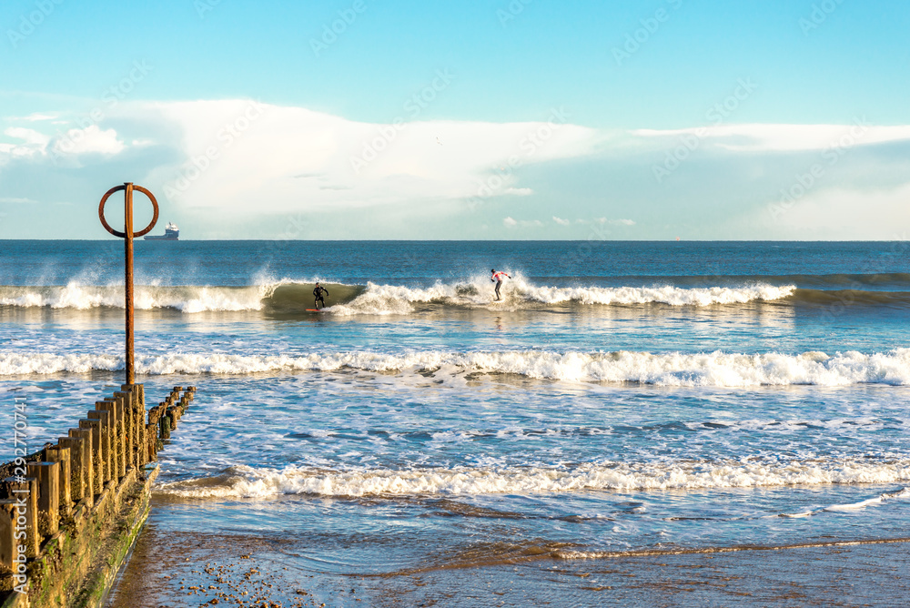 Two surfers enjoy board ride on North sea waves at Aberdeen city beach, Scotland