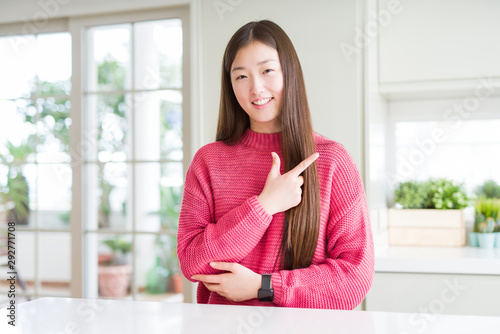 Free Download Beautiful Asian woman wearing pink sweater on white table cheerful with a smile of face pointing with hand and finger up to the side with happy and natural expression on face - GFXLoad