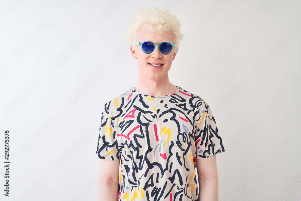Young albino blond man wearing colorful t-shirt and sunglasses over isolated red background with a happy and cool smile on face. Lucky person.