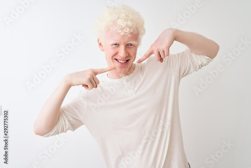 Young albino blond man wearing casual t-shirt standing over isolated white background smiling cheerful showing and pointing with fingers teeth and mouth. Dental health concept.