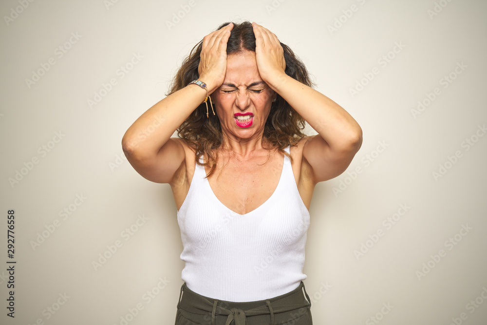 Middle age senior woman standing over white isolated background suffering from headache desperate and stressed because pain and migraine. Hands on head. Middle age senior woman standing over white isolated background suffering from headache desperate and stressed because pain and migraine. Hands on head.