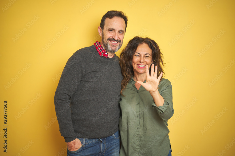Beautiful middle age couple over isolated yellow background showing and pointing up with fingers number five while smiling confident and happy. Beautiful middle age couple over isolated yellow background showing and pointing up with fingers number five while smiling confident and happy.