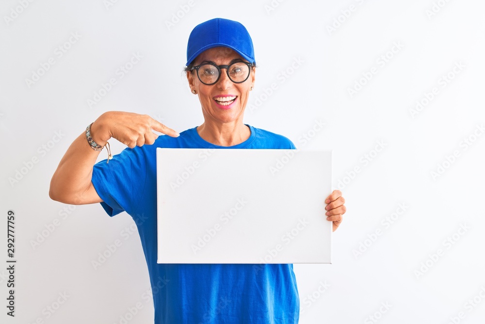 Senior deliverywoman wearing cap and glasses holding banner over isolated white background with surprise face pointing finger to himself Senior deliverywoman wearing cap and glasses holding banner over isolated white background with surprise face pointing finger to himself