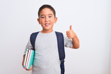 Beautiful student kid boy wearing backpack holding books over isolated white background happy with big smile doing ok sign, thumb up with fingers, excellent sign