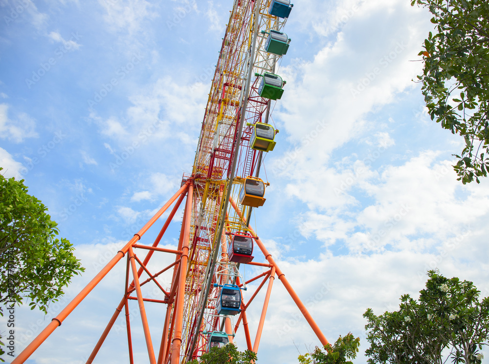 Ferris wheel attraction in summer park. Orange metallic construction of attraction. Colorful car on ferris wheel. Ferris wheel attraction in summer park. Orange metallic construction of attraction. Colorful car on ferris wheel.