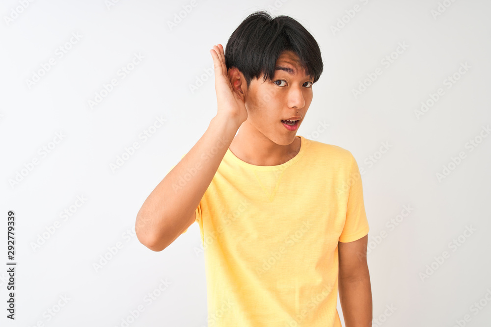 Chinese man wearing yellow casual t-shirt standing over isolated white background smiling with hand over ear listening an hearing to rumor or gossip. Deafness concept. Chinese man wearing yellow casual t-shirt standing over isolated white background smiling with hand over ear listening an hearing to rumor or gossip. Deafness concept.