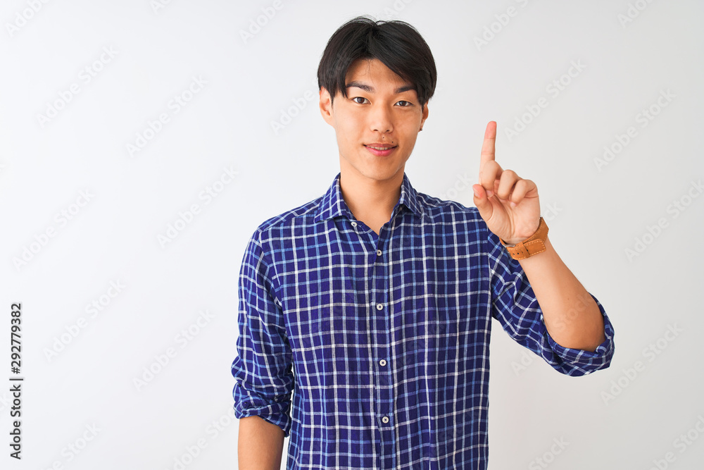 Young chinese man wearing casual blue shirt standing over isolated white background showing and pointing up with finger number one while smiling confident and happy. Young chinese man wearing casual blue shirt standing over isolated white background showing and pointing up with finger number one while smiling confident and happy.