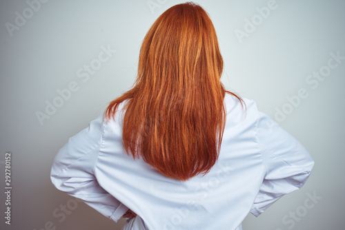 Young redhead doctor woman using stethoscope over white isolated background standing backwards looking away with arms on body