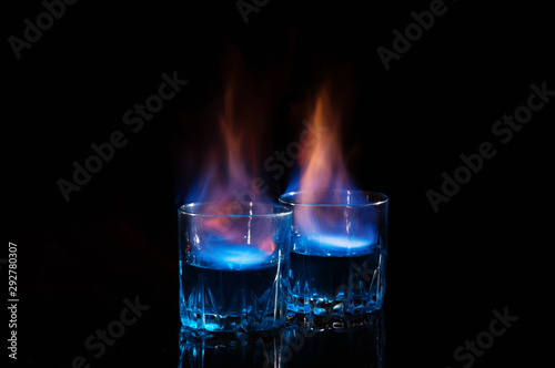 Close up, macro. Two glass glasses with blue alcohol with a flame of burning fire. Black background. Copy space.