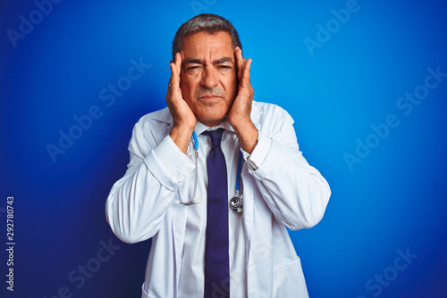 Handsome middle age doctor man wearing stethoscope over isolated blue background with hand on head for pain in head because stress. Suffering migraine. © Krakenimages.com