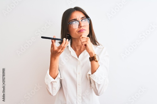 Woman wearing glasses sending message on smartphone over isolated white background serious face thinking about question, very confused idea