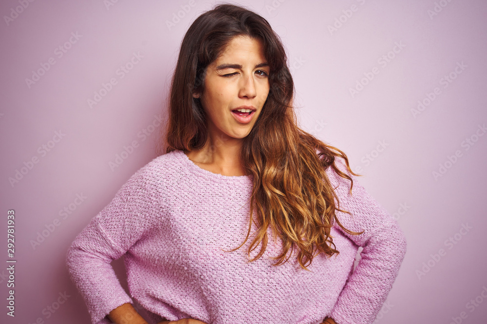Young beautiful woman wearing sweater standing over pink isolated background winking looking at the camera with sexy expression, cheerful and happy face. Young beautiful woman wearing sweater standing over pink isolated background winking looking at the camera with sexy expression, cheerful and happy face.