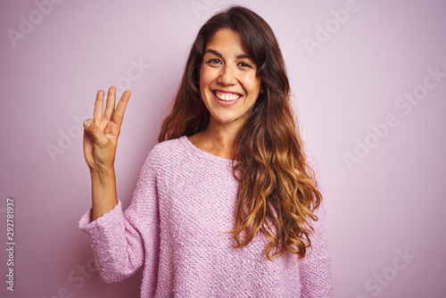 Young beautiful woman wearing sweater standing over pink isolated background showing and pointing up with fingers number three while smiling confident and happy.