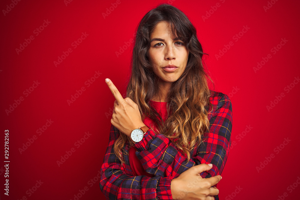 Young beautiful woman wearing casual jacket standing over red isolated background amazed and surprised looking up and pointing with fingers and raised arms. Young beautiful woman wearing casual jacket standing over red isolated background amazed and surprised looking up and pointing with fingers and raised arms.