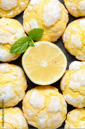 Background of freshly backed cracked crinkle Lemon cookies and slice of fresh lemon and mint leaf on dark background. Close up. Top view, vertical composition photo