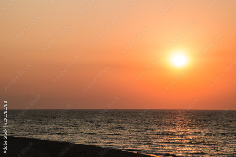 Sunrise on the beach, orange-red gradient in the sky. Copy space.