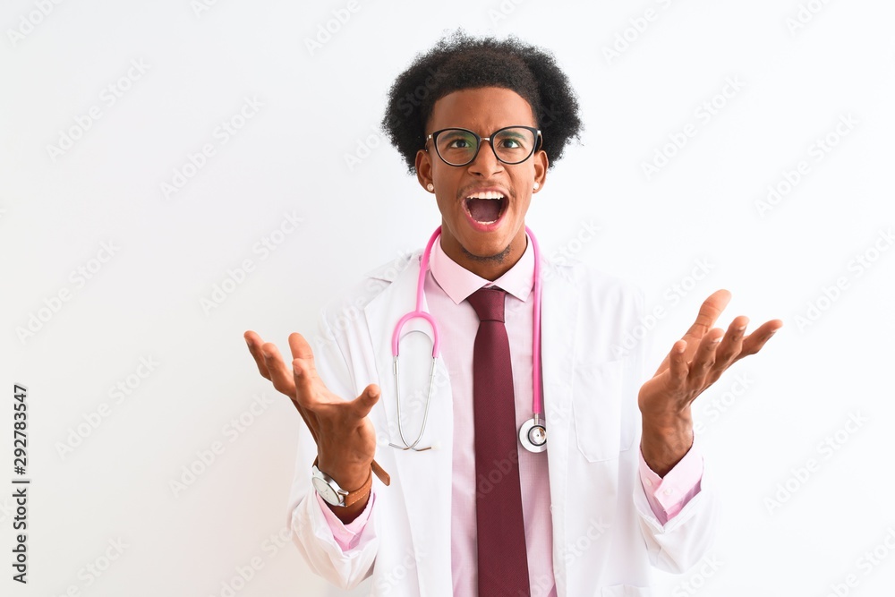 Young african american doctor man wearing pink stethoscope over isolated white background crazy and mad shouting and yelling with aggressive expression and arms raised. Frustration concept. Young african american doctor man wearing pink stethoscope over isolated white background crazy and mad shouting and yelling with aggressive expression and arms raised. Frustration concept.