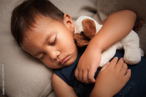A young male child who fell sleep during the daytime while hugging his stuffed animal toy.
