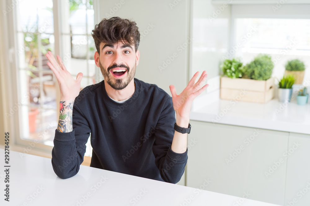 Young man wearing casual sweatshirt sitting on white table celebrating crazy and amazed for success with arms raised and open eyes screaming excited. Winner concept Young man wearing casual sweatshirt sitting on white table celebrating crazy and amazed for success with arms raised and open eyes screaming excited. Winner concept