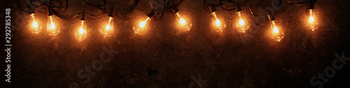 Row of lit string light bulbs glowing on dark grungy background.