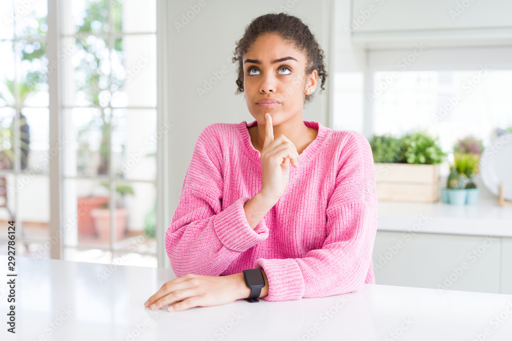 Beautiful african american woman with afro hair wearing casual pink sweater Thinking concentrated about doubt with finger on chin and looking up wondering Beautiful african american woman with afro hair wearing casual pink sweater Thinking concentrated about doubt with finger on chin and looking up wondering