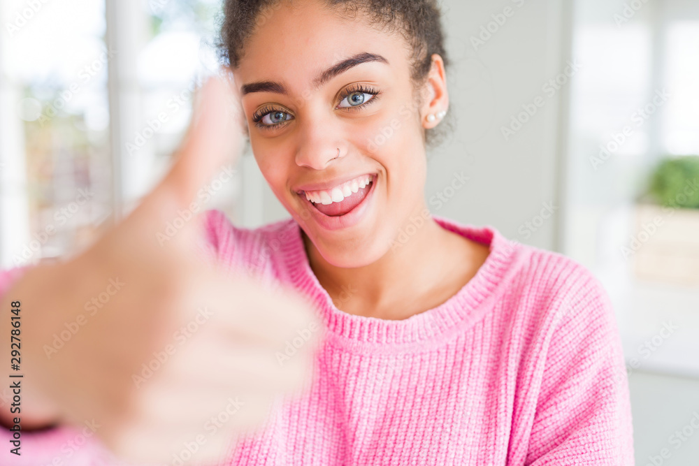 Beautiful young african american woman with afro hair doing happy thumbs up gesture with hand. Approving expression looking at the camera showing success. Beautiful young african american woman with afro hair doing happy thumbs up gesture with hand. Approving expression looking at the camera showing success.