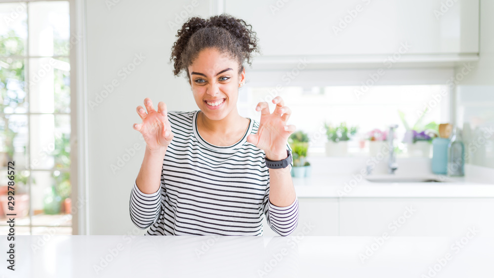 Beautiful african american woman with afro hair wearing casual striped sweater smiling funny doing claw gesture as cat, aggressive and sexy expression Beautiful african american woman with afro hair wearing casual striped sweater smiling funny doing claw gesture as cat, aggressive and sexy expression
