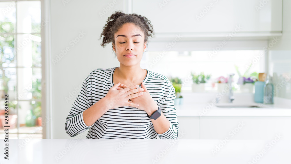 Beautiful african american woman with afro hair wearing casual striped sweater smiling with hands on chest with closed eyes and grateful gesture on face. Health concept. Beautiful african american woman with afro hair wearing casual striped sweater smiling with hands on chest with closed eyes and grateful gesture on face. Health concept.