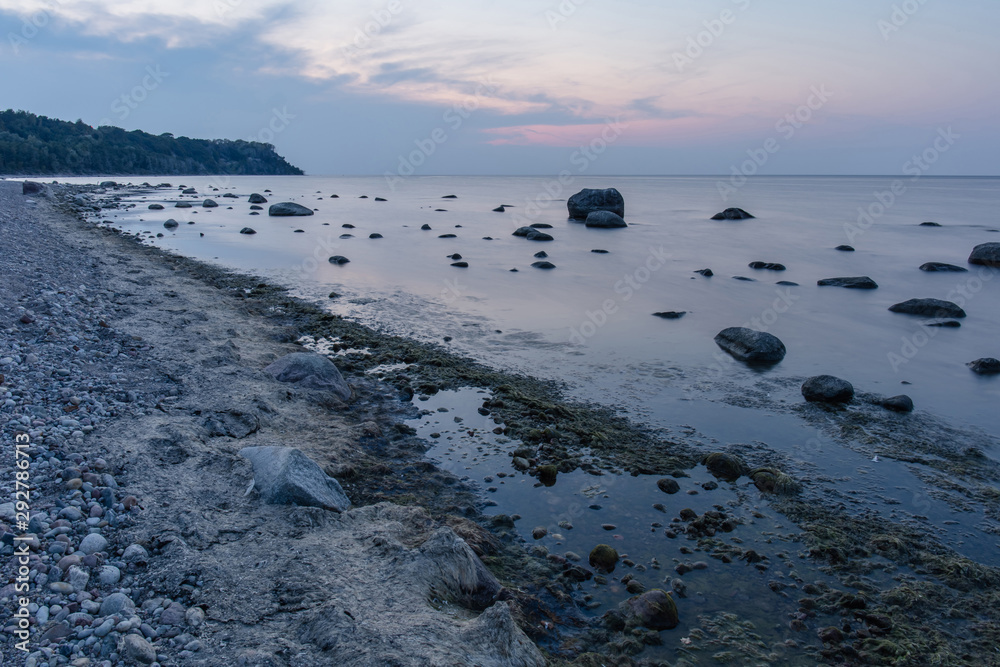 Fototapeta premium seascape with rocky beach covered with mud, large boulders in the water in blue twilight