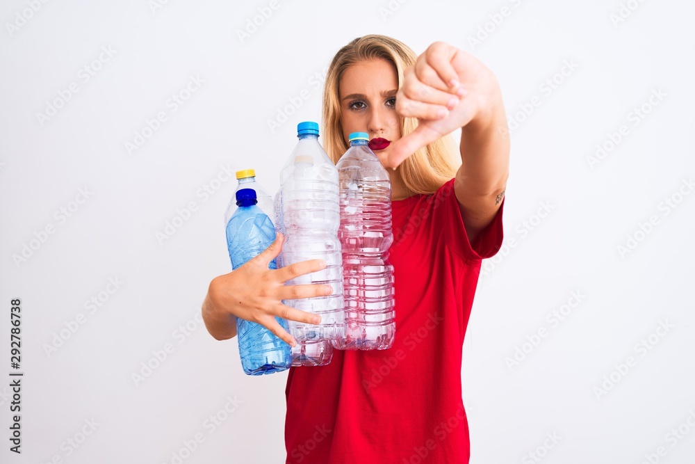 Young beautiful woman recycling plastic bottles standing over isolated white background with angry face, negative sign showing dislike with thumbs down, rejection concept Young beautiful woman recycling plastic bottles standing over isolated white background with angry face, negative sign showing dislike with thumbs down, rejection concept