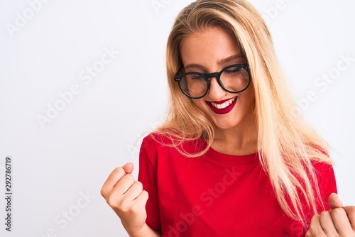 Young beautiful woman wearing red t-shirt and glasses standing over isolated white background very happy and excited doing winner gesture with arms raised  smiling and screaming for success