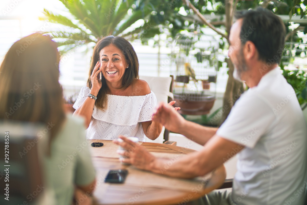 Beautiful family sitting on terrace drinking cup of coffee talking on the smartphone and smiling Beautiful family sitting on terrace drinking cup of coffee talking on the smartphone and smiling
