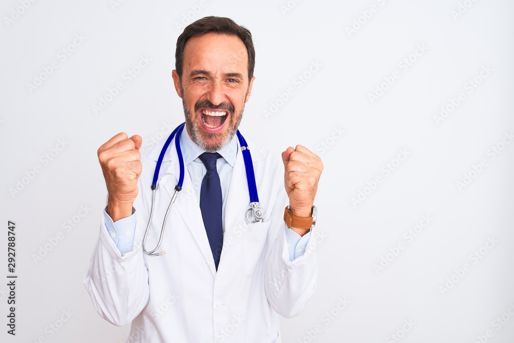 Middle age doctor man wearing coat and stethoscope standing over isolated white background celebrating surprised and amazed for success with arms raised and open eyes. Winner concept. Middle age doctor man wearing coat and stethoscope standing over isolated white background celebrating surprised and amazed for success with arms raised and open eyes. Winner concept.