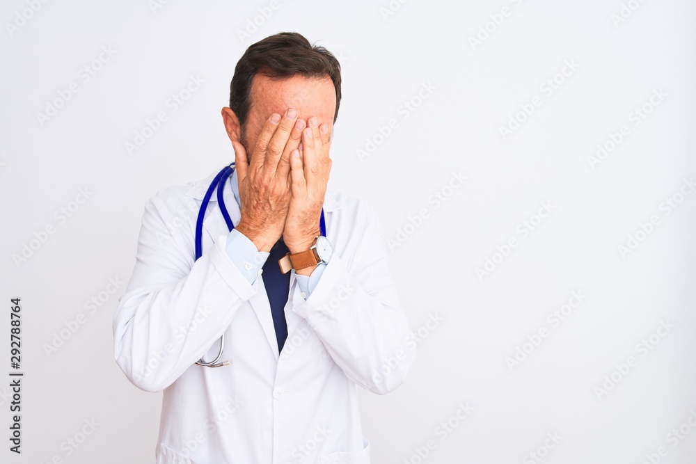 Middle age doctor man wearing coat and stethoscope standing over isolated white background with sad expression covering face with hands while crying. Depression concept. Middle age doctor man wearing coat and stethoscope standing over isolated white background with sad expression covering face with hands while crying. Depression concept.