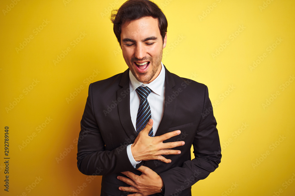 Young handsome businessman wearing suit and tie standing over isolated yellow background smiling and laughing hard out loud because funny crazy joke with hands on body. Young handsome businessman wearing suit and tie standing over isolated yellow background smiling and laughing hard out loud because funny crazy joke with hands on body.