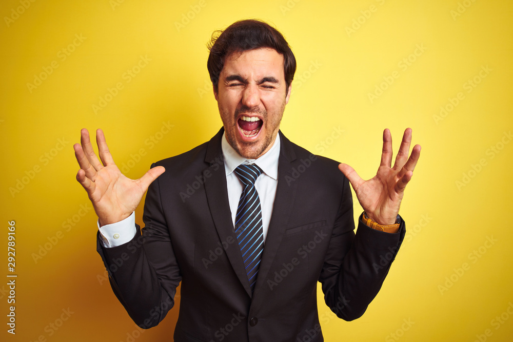 Young handsome businessman wearing suit and tie standing over isolated yellow background celebrating mad and crazy for success with arms raised and closed eyes screaming excited. Winner concept Young handsome businessman wearing suit and tie standing over isolated yellow background celebrating mad and crazy for success with arms raised and closed eyes screaming excited. Winner concept