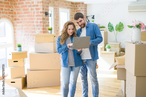 Young couple using computer laptop standing on a room around cardboard boxes, happy for moving to a new apartment © Krakenimages.com