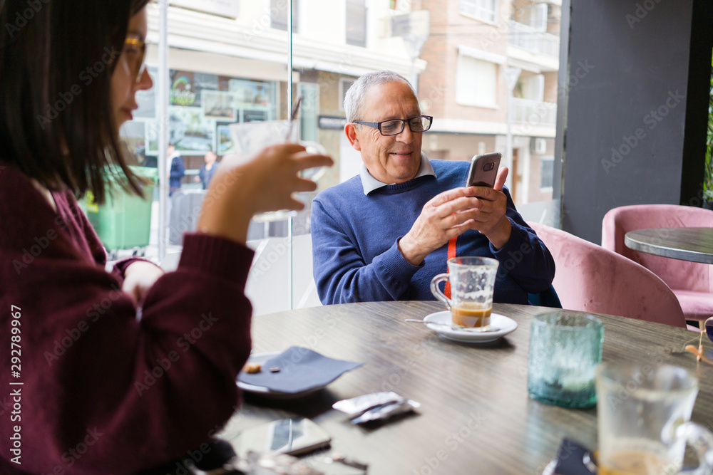 Senior man having a conversation with woman drinking coffee using smartphone and relaxing, chatting at restaurant