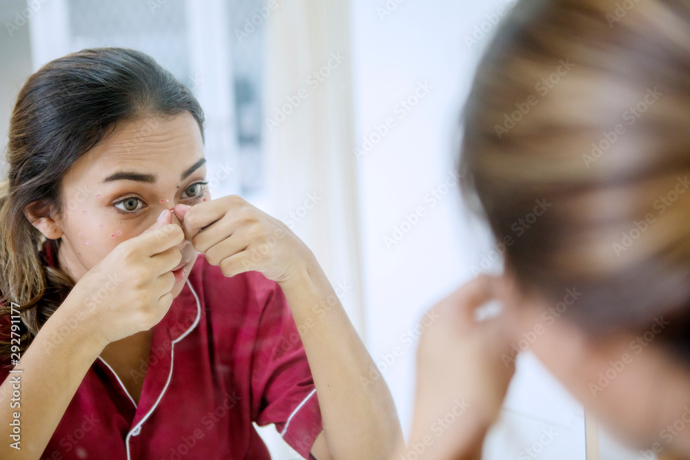 Teenage girl touching pimples in front of the mirror Teenage girl touching pimples in front of the mirror