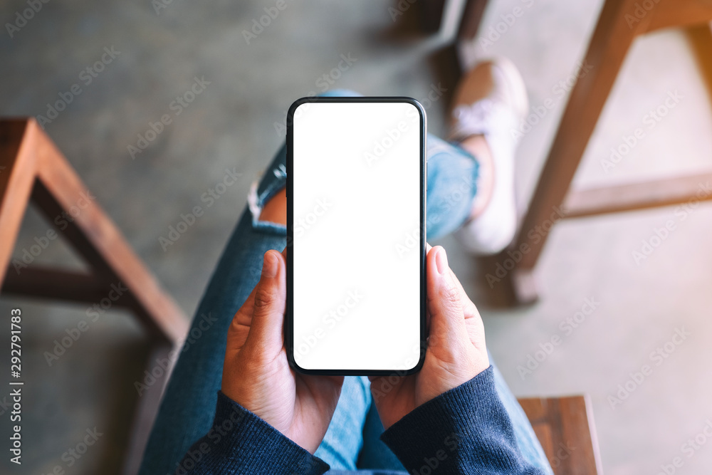 Top view mockup image of a woman holding black mobile phone with blank white screen while sitting in cafe - obrazy, fototapety, plakaty 
