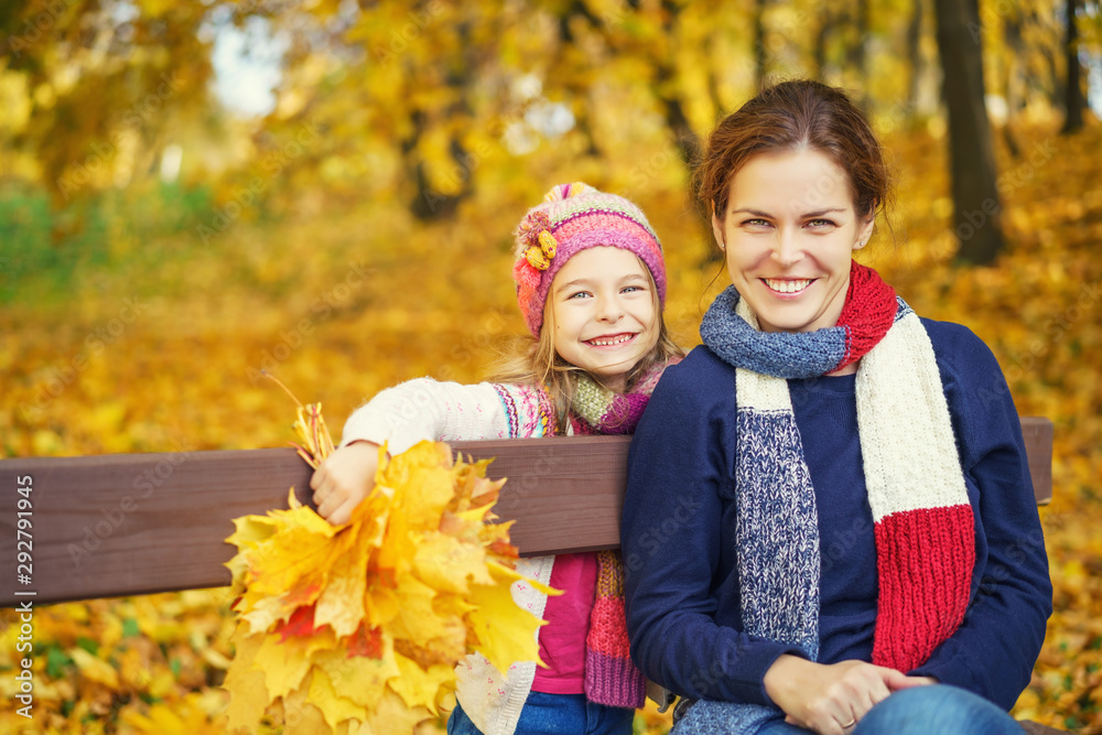 Happy little girl and her mother have fun sitting on the bench in autumn park Happy little girl and her mother have fun sitting on the bench in autumn park