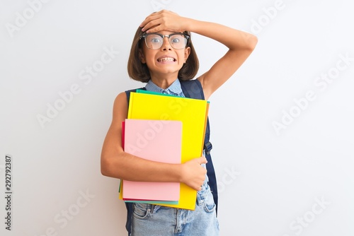 Beautiful student child girl wearing backpack glasses books over isolated white background stressed with hand on head, shocked with shame and surprise face, angry and frustrated. Fear and upset.