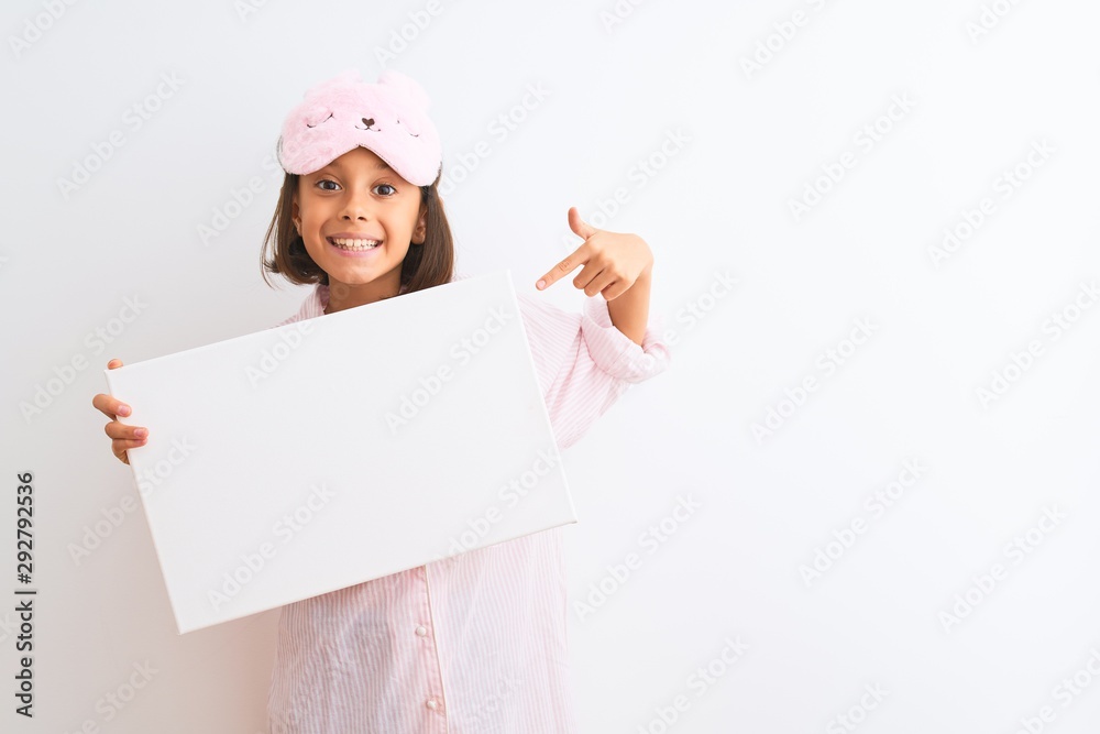 Child girl wearing sleep mask and pajama holding banner over isolated white background very happy pointing with hand and finger Child girl wearing sleep mask and pajama holding banner over isolated white background very happy pointing with hand and finger