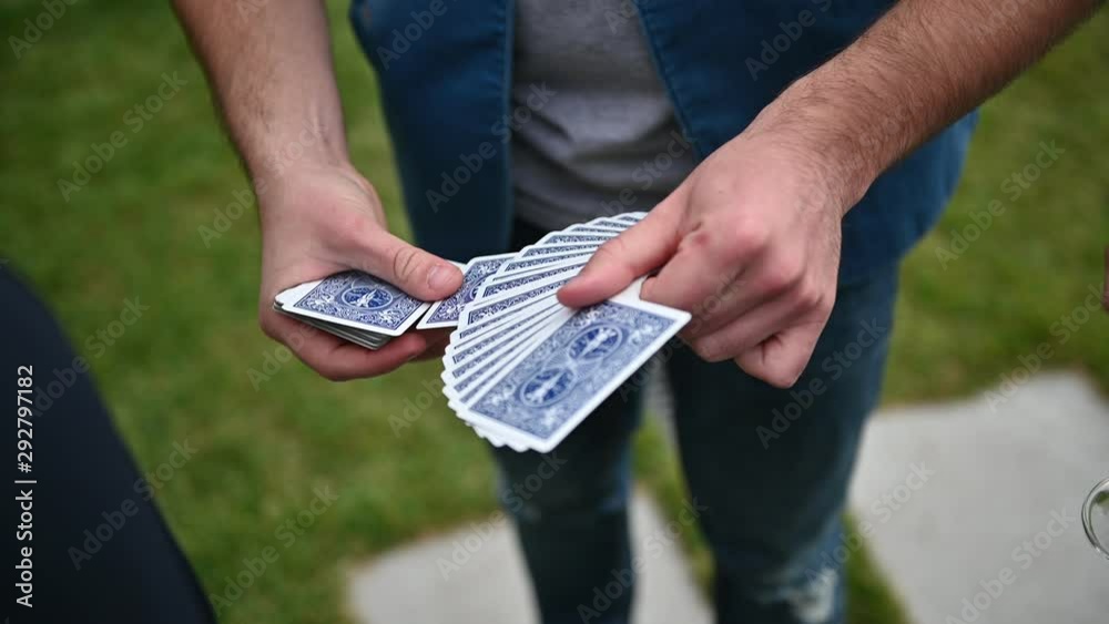 Close up illusionist in red shirt perform playing cards magic tricks. Summer day