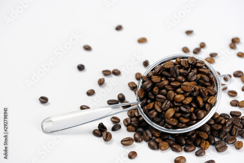 Roasted coffee seeds in metal colander on white background.